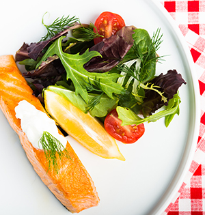 Decadent Dilled Salmon made with Astro yogurt served on a white plate alongside a green salad with cherry tomatoes