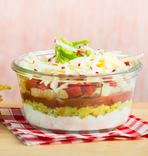 Mexican Dip made with Astro yogurt and served in a glass dish sitting on a read and white dish towel